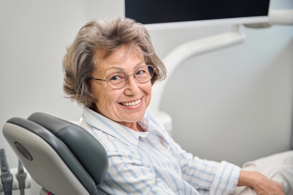 A dentist, wearing personal protective equiptment is consulting with a patient about a dental implant, using a digital scan of the patients mouth to show the implant placement. No text on the image.